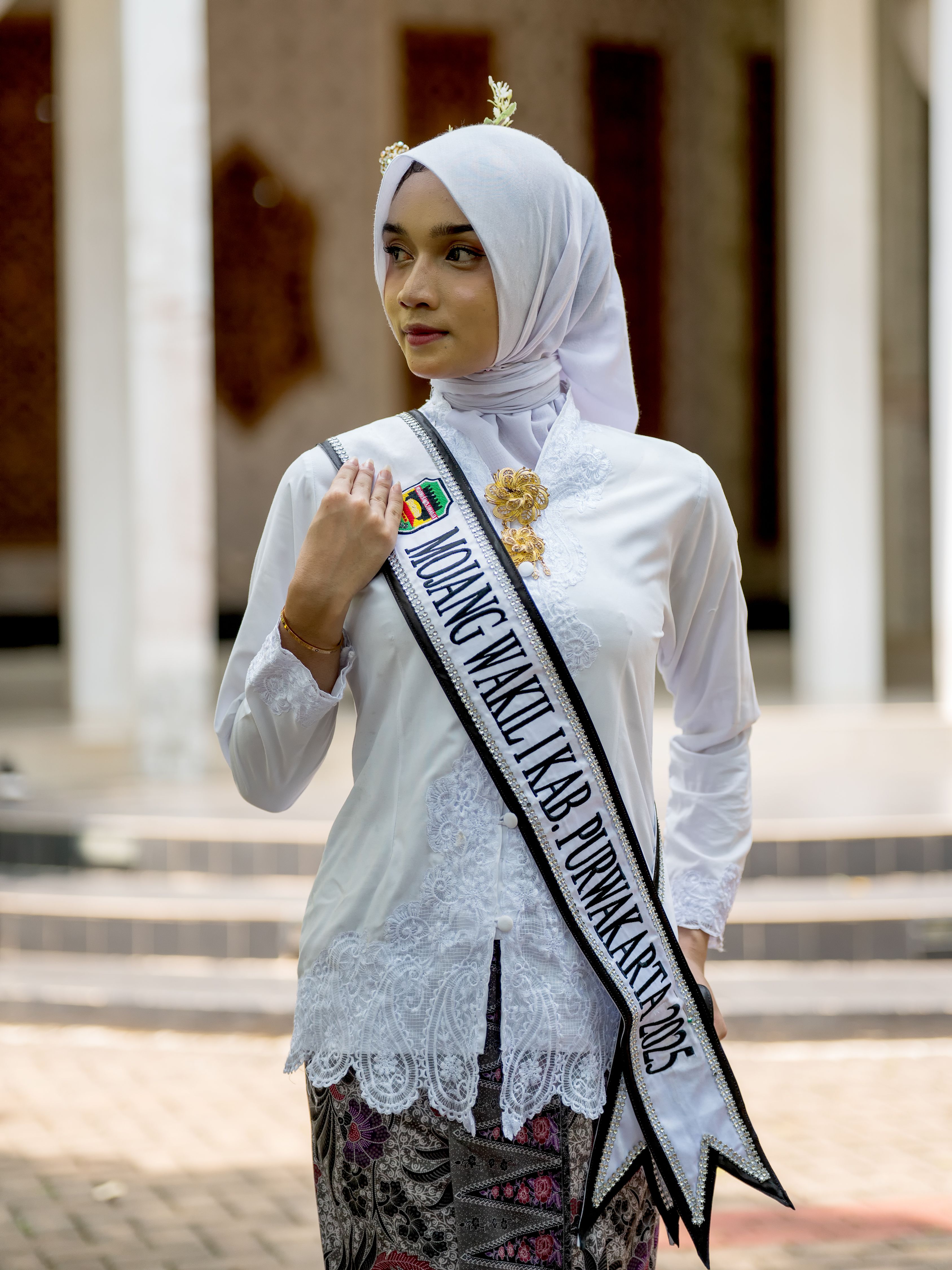 Portrait of a young woman wearing traditional attire and a sash outdoors.