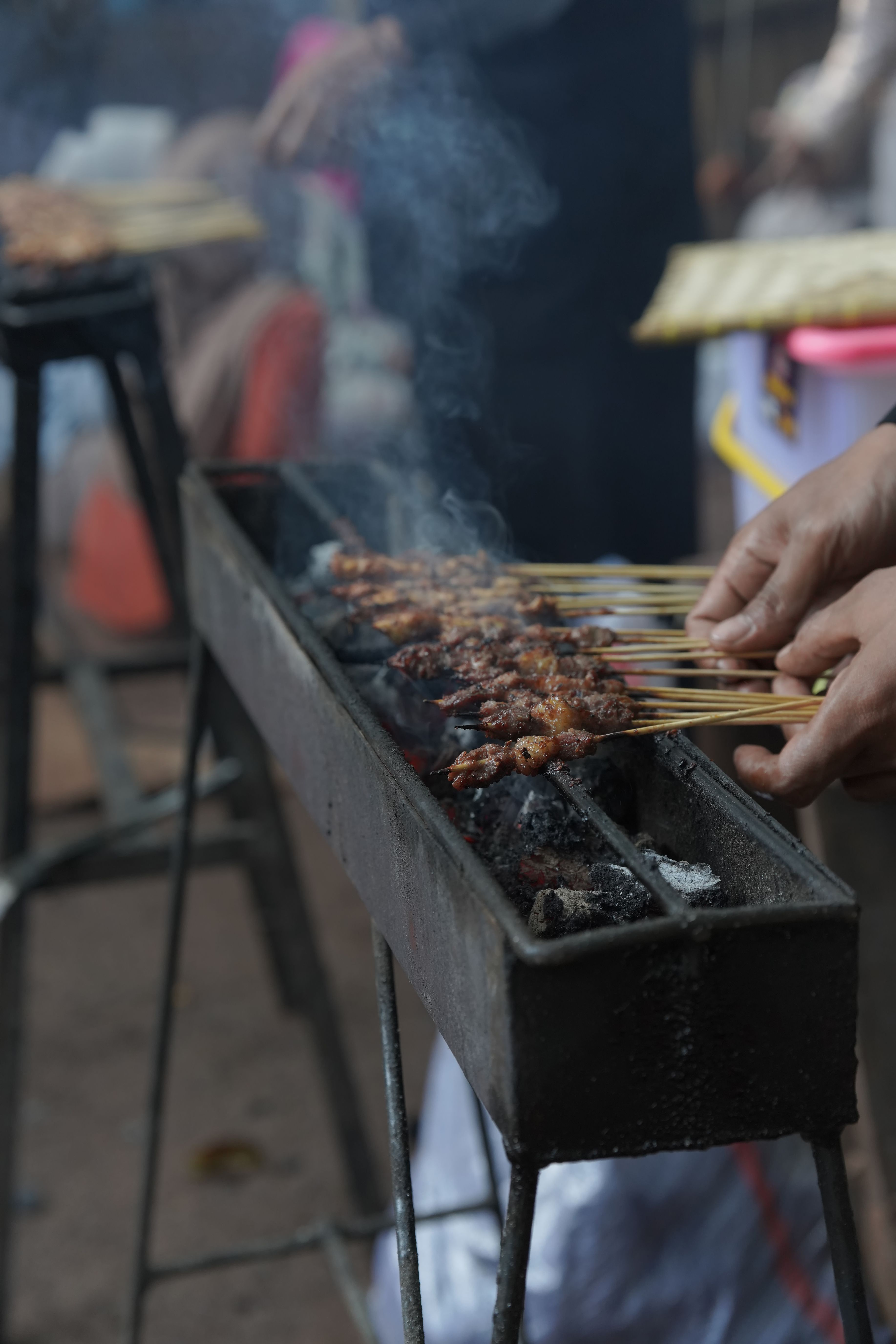 Mains d'un cuisinier disposant des brochettes de viande sur un gril à braises fumant
