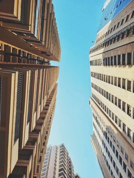 View between two towering urban skyscrapers under a clear blue sky.