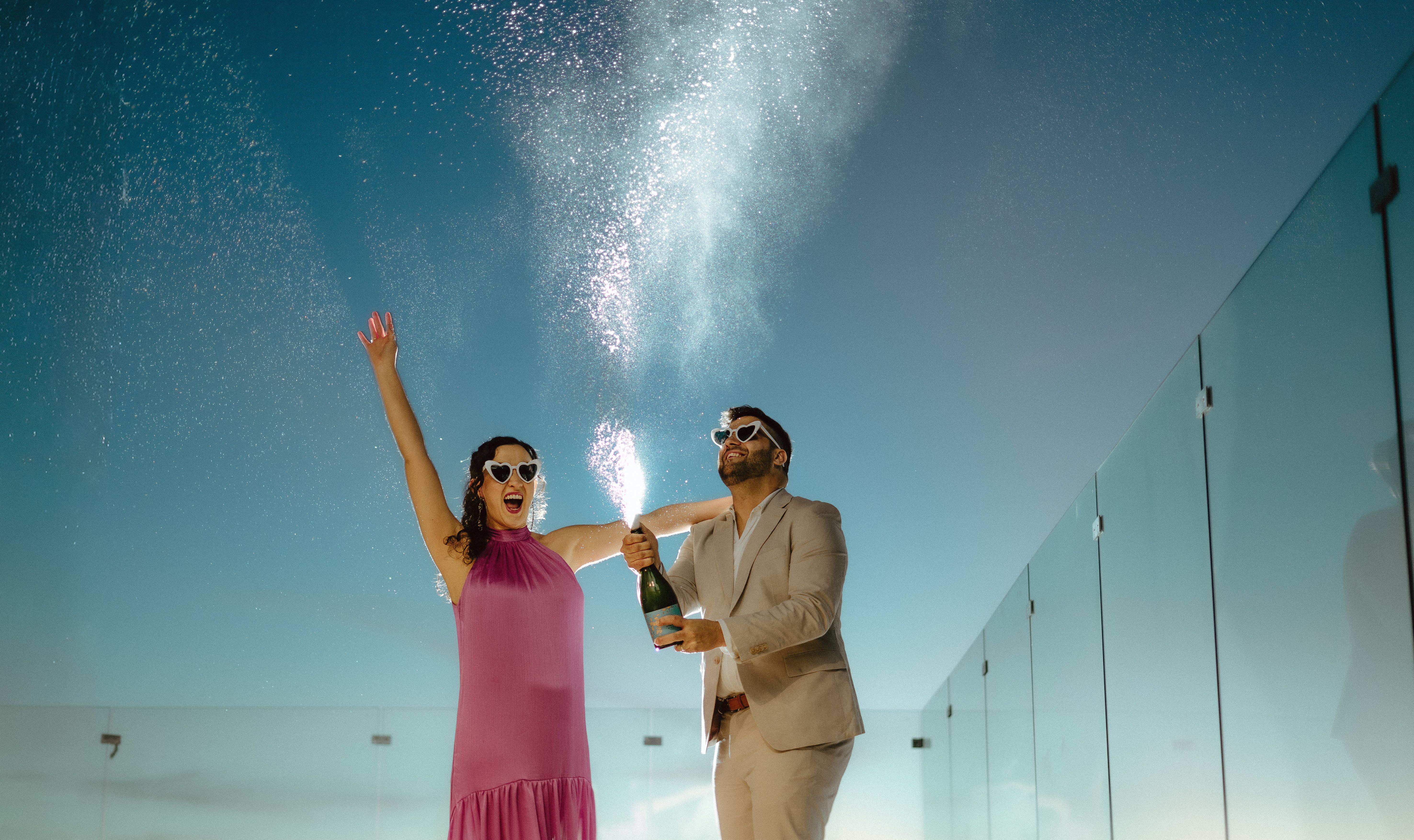 A joyful couple celebrates with champagne on a sunny rooftop.