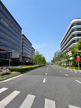 Wide empty street flanked by modern office buildings in Shanghai, China under a clear blue sky.