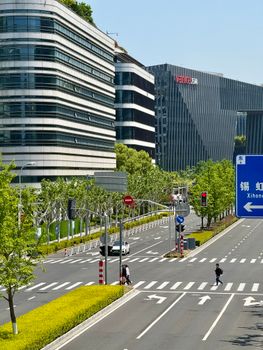 A bustling urban street in Shanghai featuring modern architecture and green spaces, captured in clear daylight.