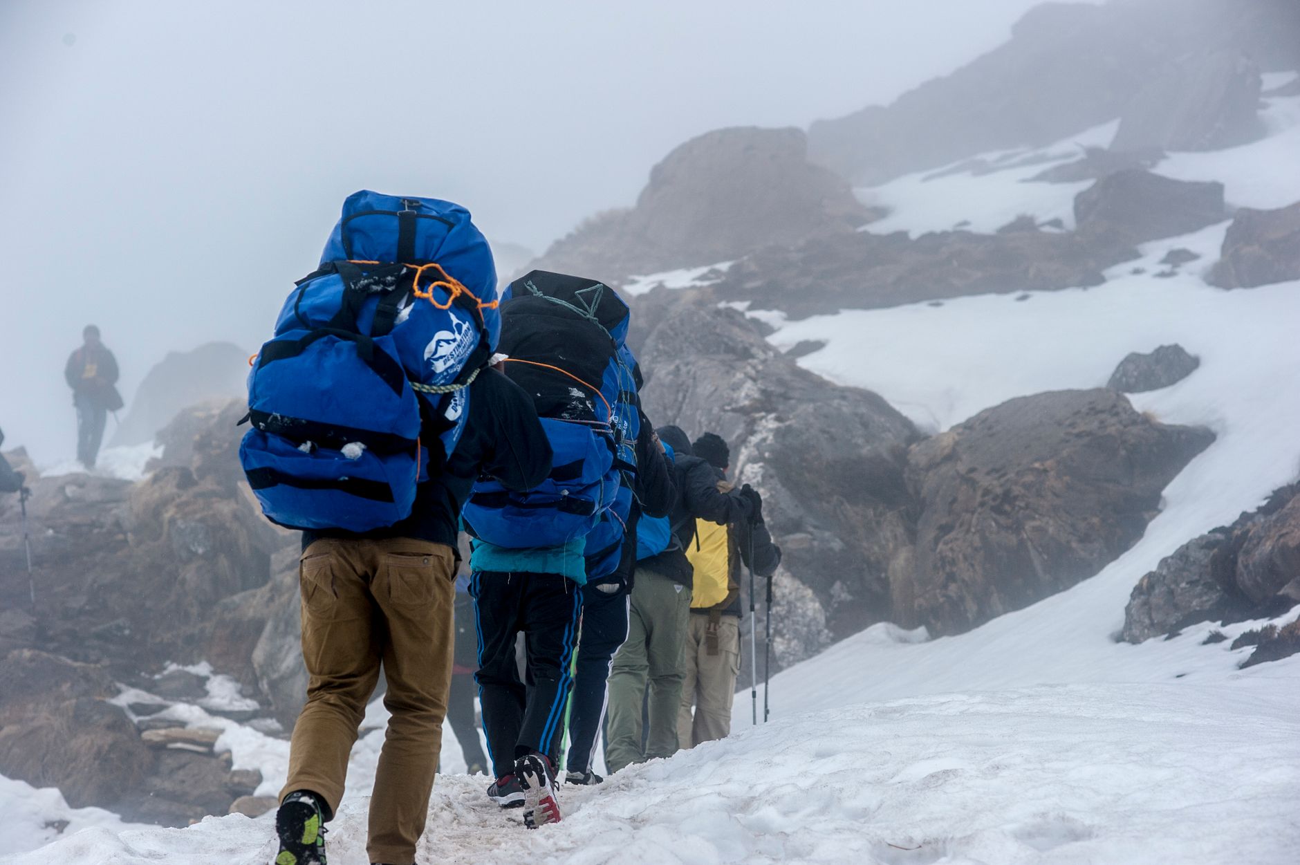 A group of hikers ascending a snowy mountain trail in Ghandruk, Nepal, during a misty day.