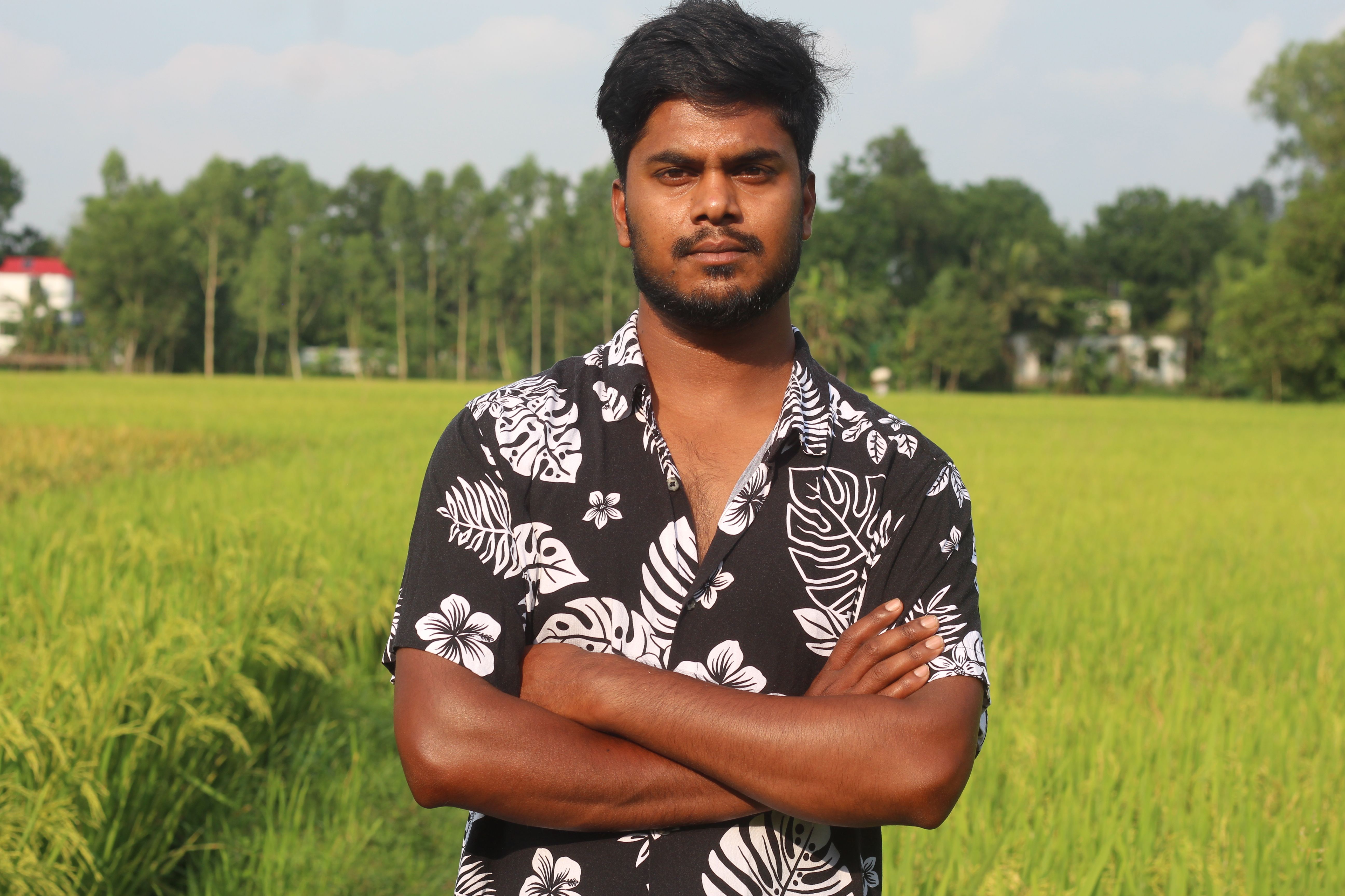 A man stands confidently in an open green field under a clear blue sky.