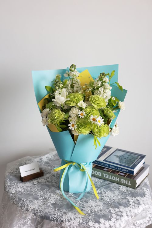 Free A beautiful bouquet with green and white flowers wrapped in blue paper, resting on a lace-covered table. Stock Photo