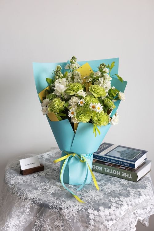 Free A delicate bouquet of green and white flowers beautifully wrapped, sitting on a lace-covered table. Stock Photo