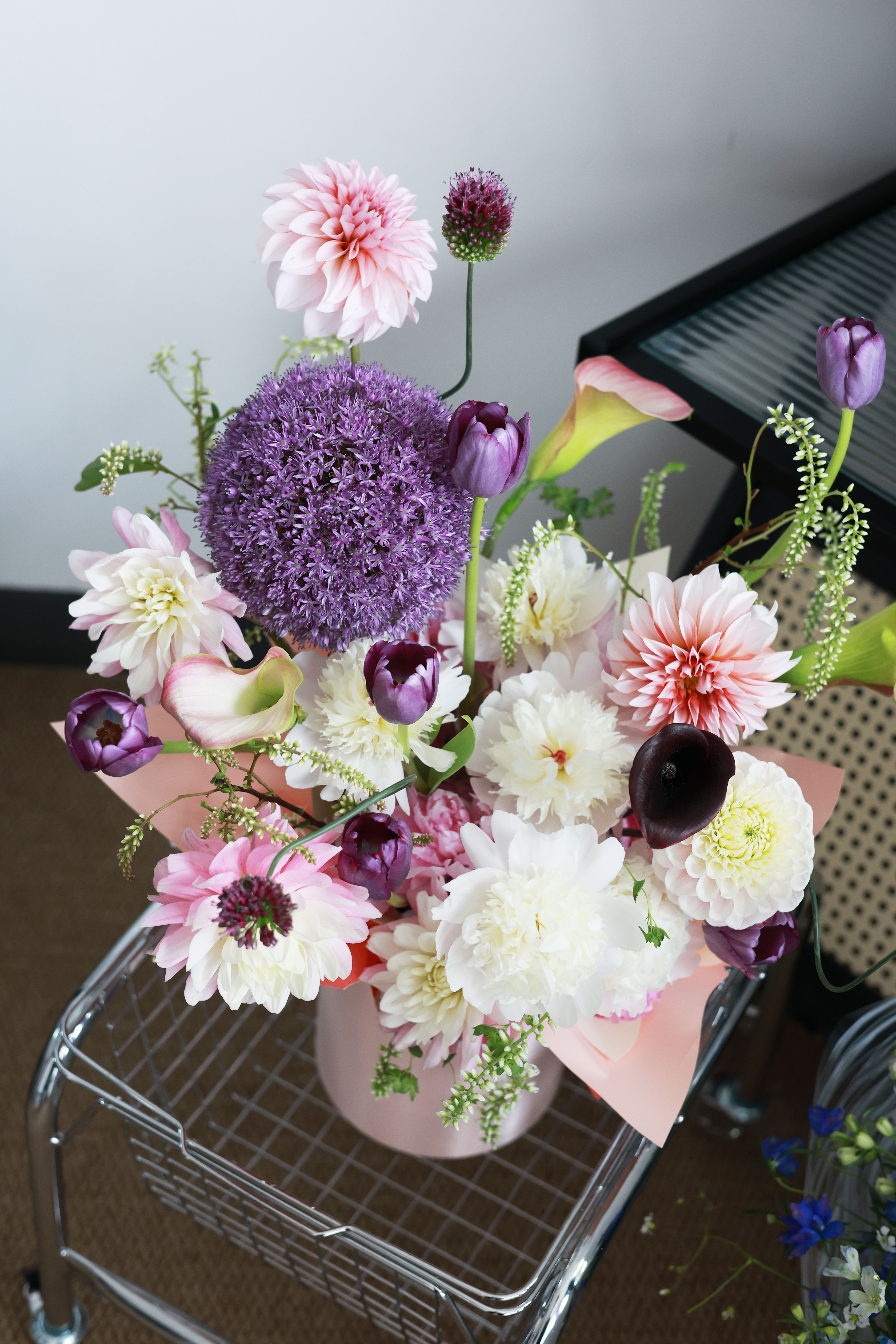 A beautiful floral arrangement featuring colorful dahlias, alliums, and tulips in a modern setting.
