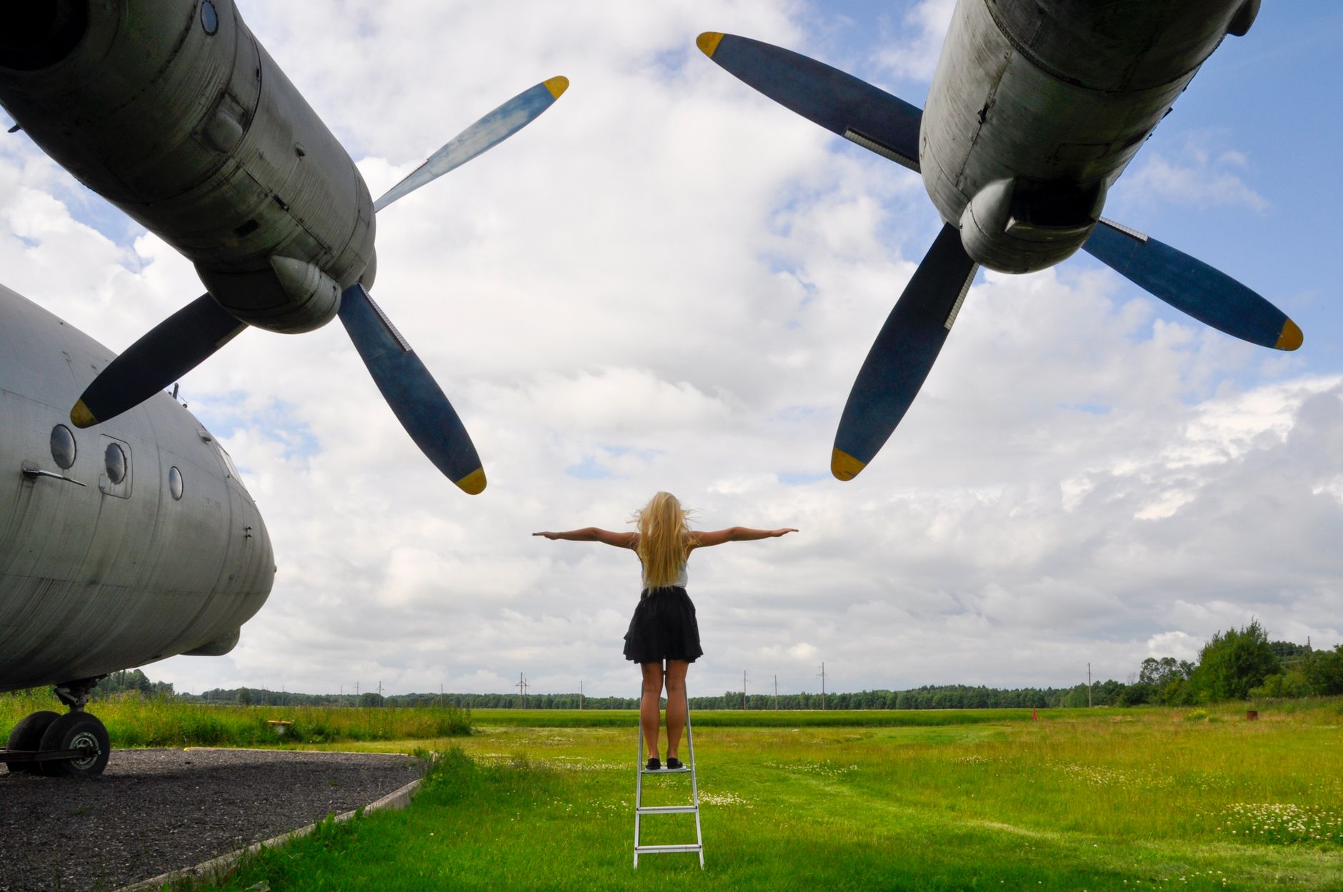 A woman with outstretched arms stands on a ladder between vintage aircraft in Keila, Estonia.