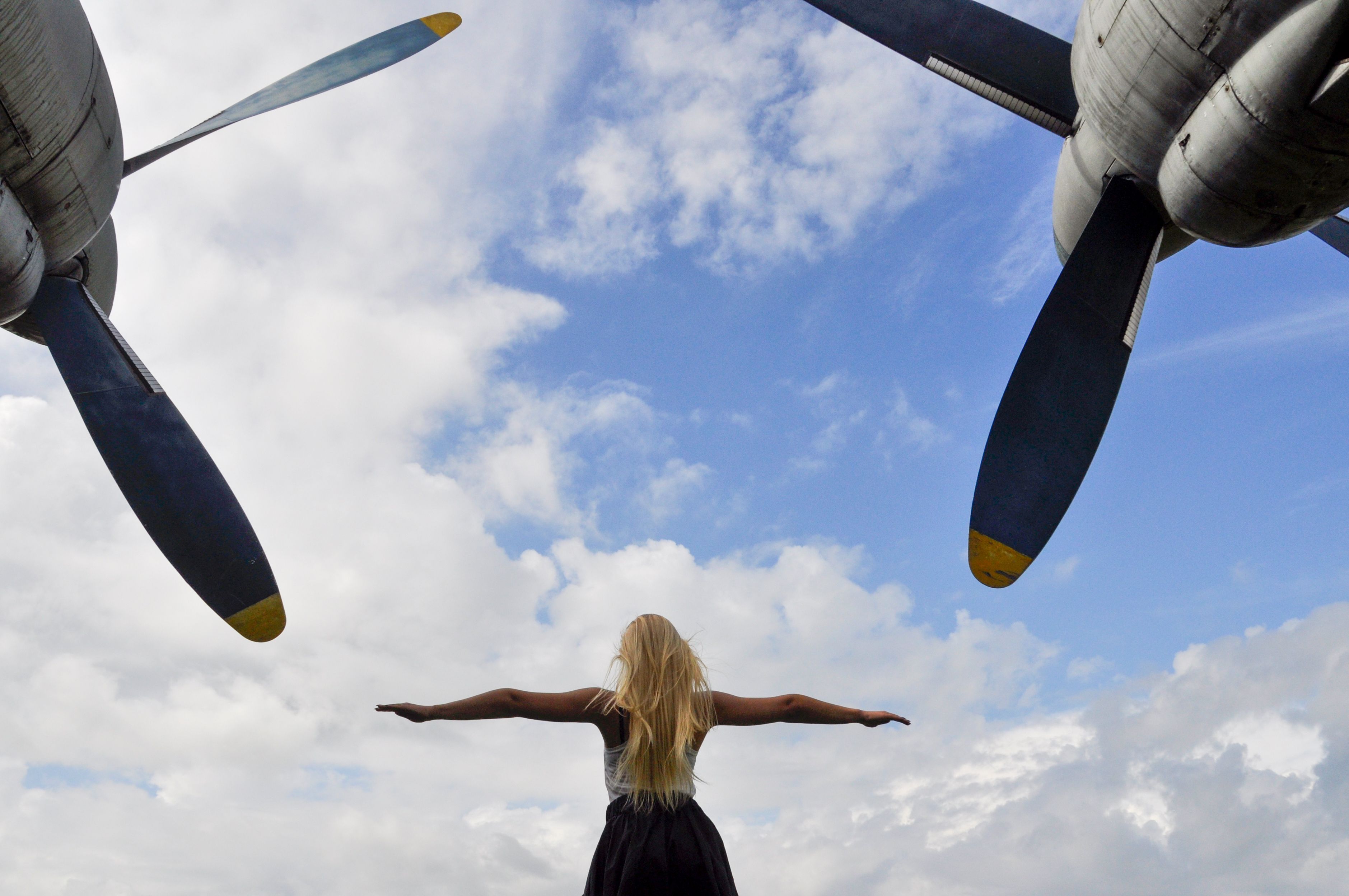 Woman with outstretched arms under blue sky and vintage propellers in Estonia.