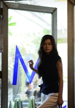 Portrait of a young woman standing indoors by a glass door with blue decor, exuding a modern and stylish vibe.