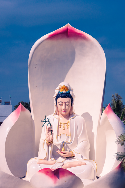 Free Serene Buddhist statue surrounded by lotus petals and blue sky backdrop. Stock Photo