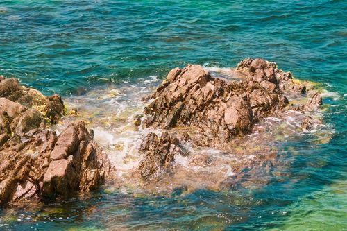 Free Rocky shoreline with vibrant blue sea creating a picturesque natural scene. Stock Photo
