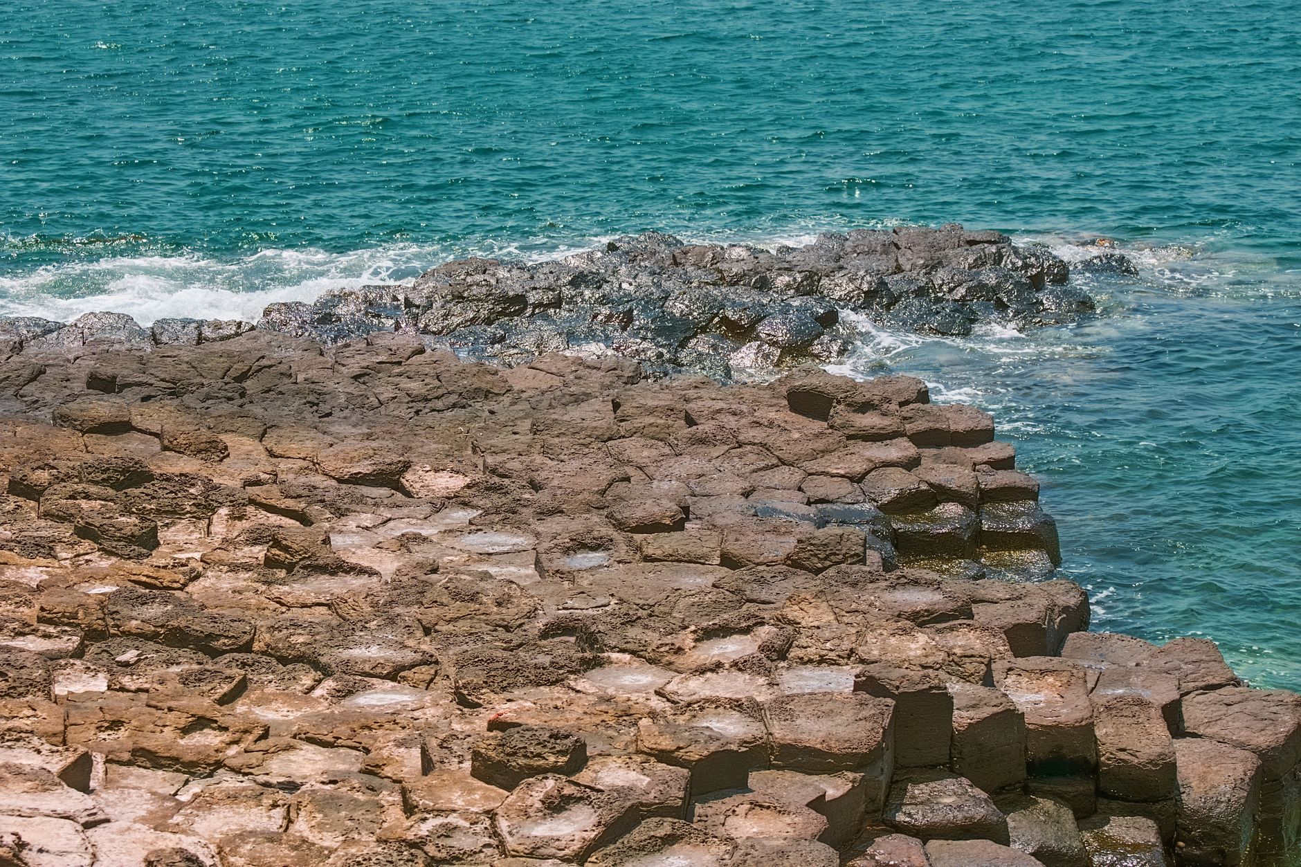 Hexagonal basalt rocks meeting ocean waves in a natural coastal scene.