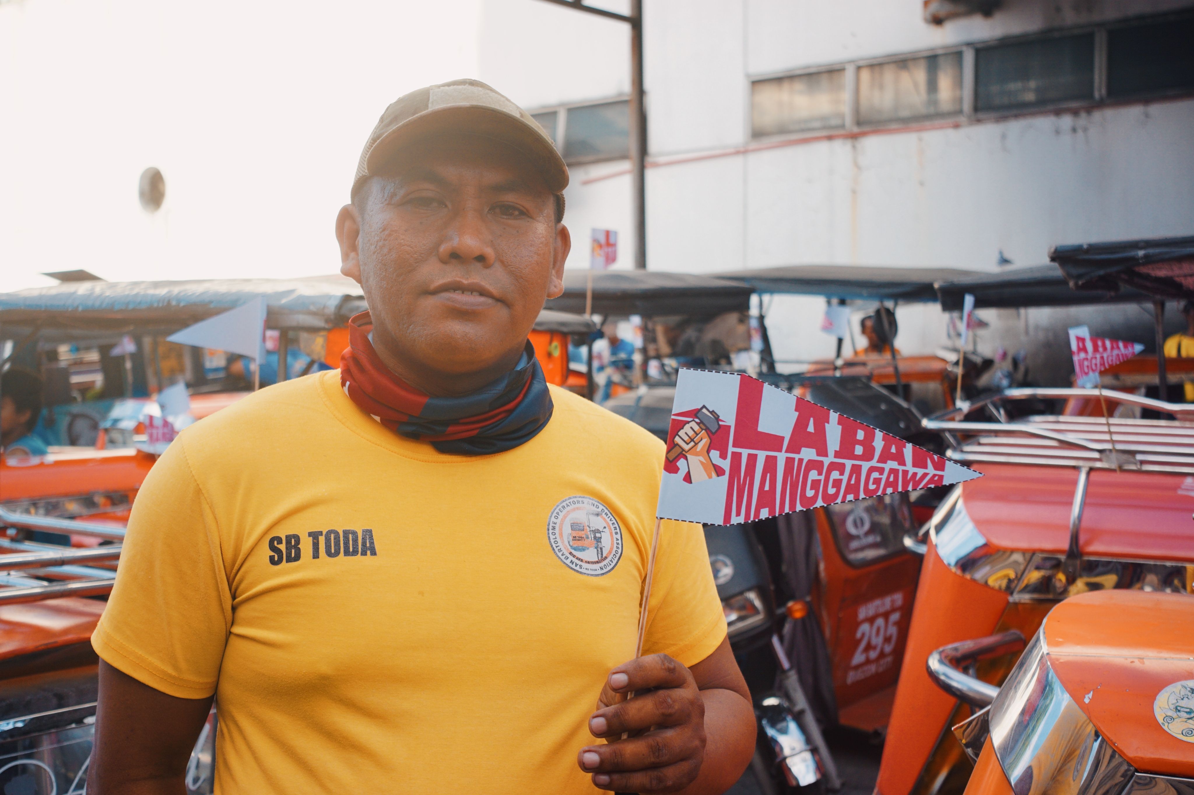 A Filipino tricycle driver holds a protest sign advocating for labor rights, standing by a line of tricycles.