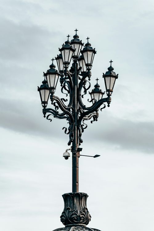 Free A detailed view of a vintage street lamp with ornate design set against a cloudy sky. Stock Photo