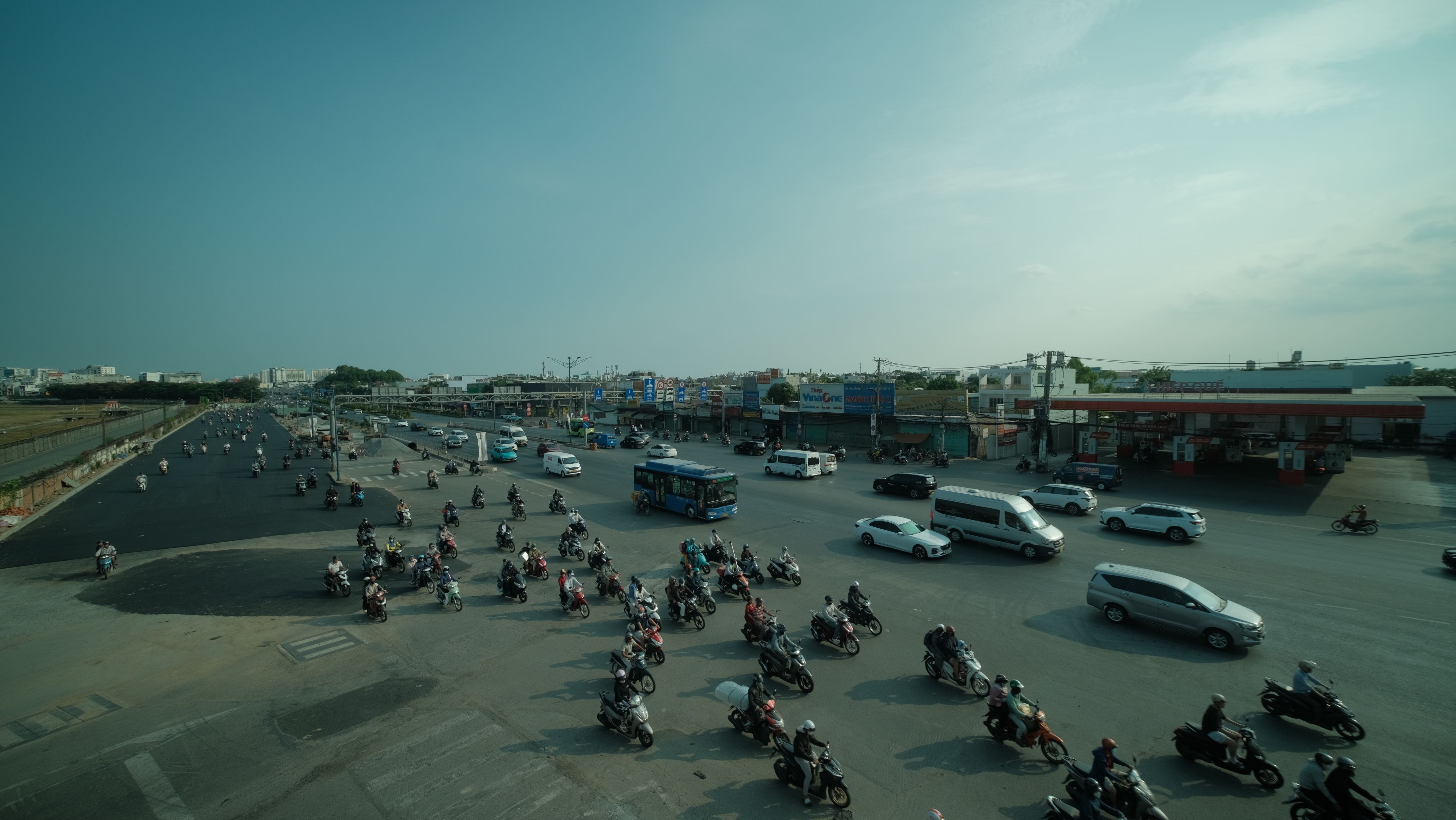 A bustling urban intersection with cars and motorbikes in Vietnam on a sunny day.