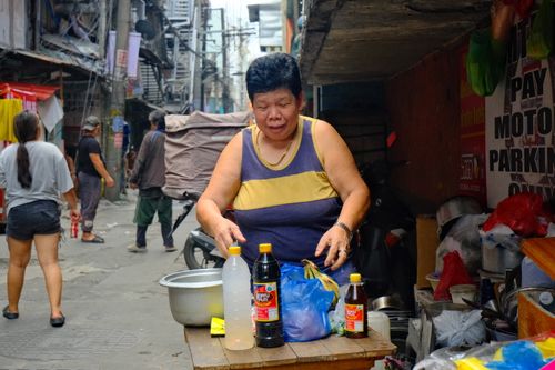 Free A street vendor in Manila prepares local condiments in a busy alleyway, showcasing daily life in the Philippines. Stock Photo