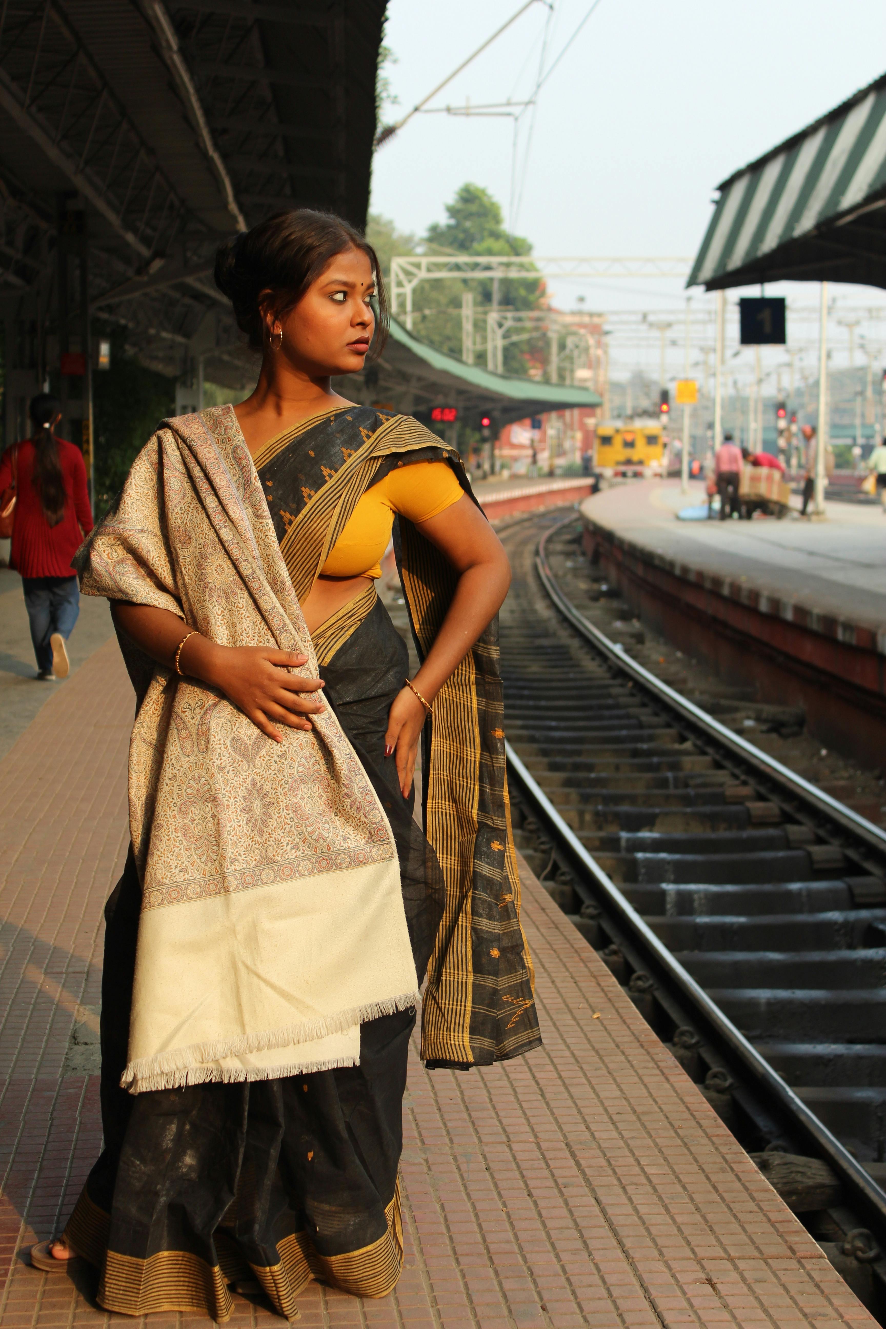 Young woman in traditional saree waiting at a bustling Kolkata train station platform.