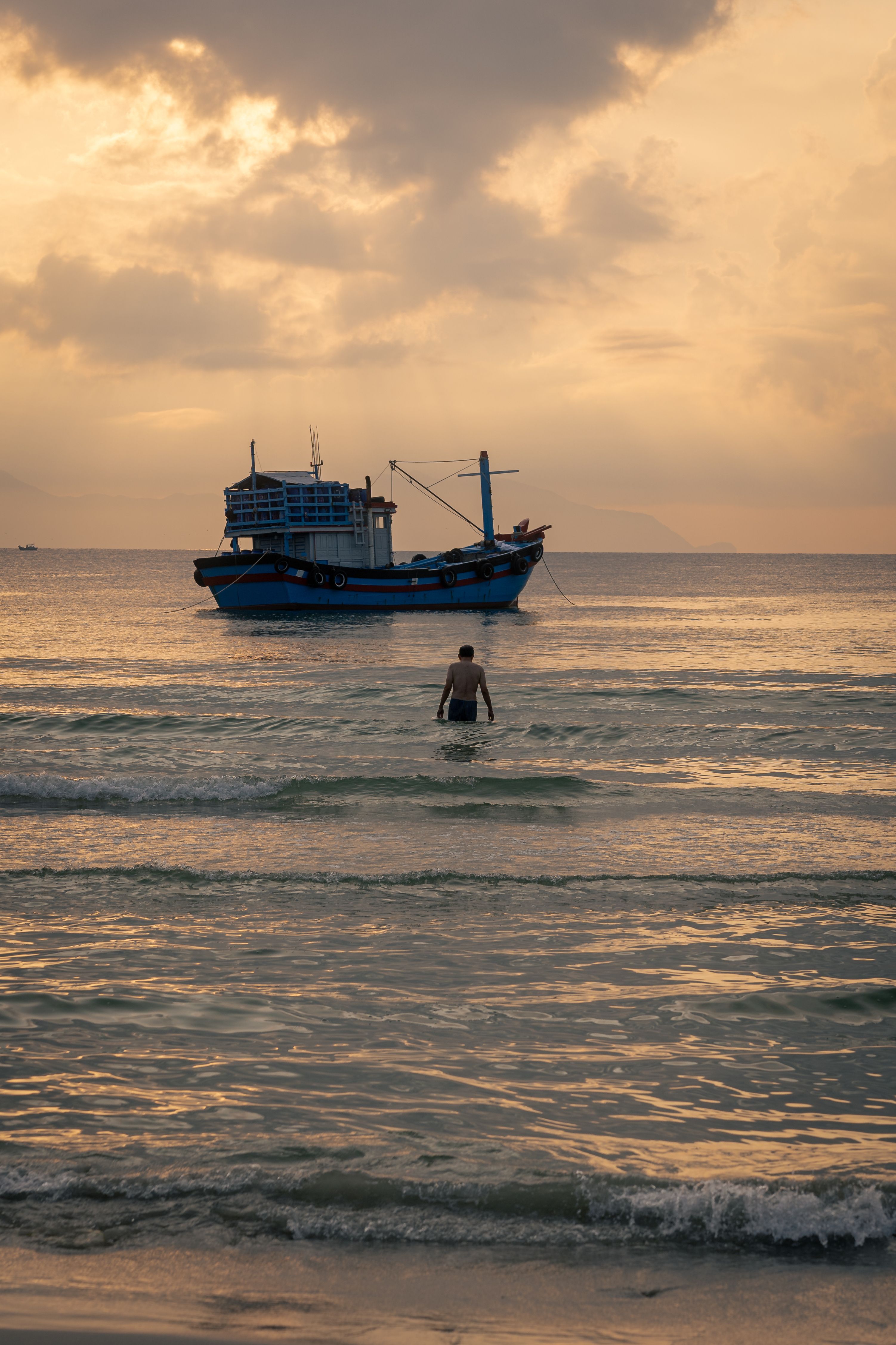 A fisherman wades towards a boat at sunrise in Đông Ninh Hòa, Vietnam.
