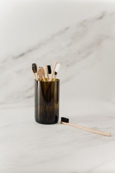 Minimalist setup of wooden toothbrushes in a dark glass holder on a marble surface, emphasizing eco-friendly living.