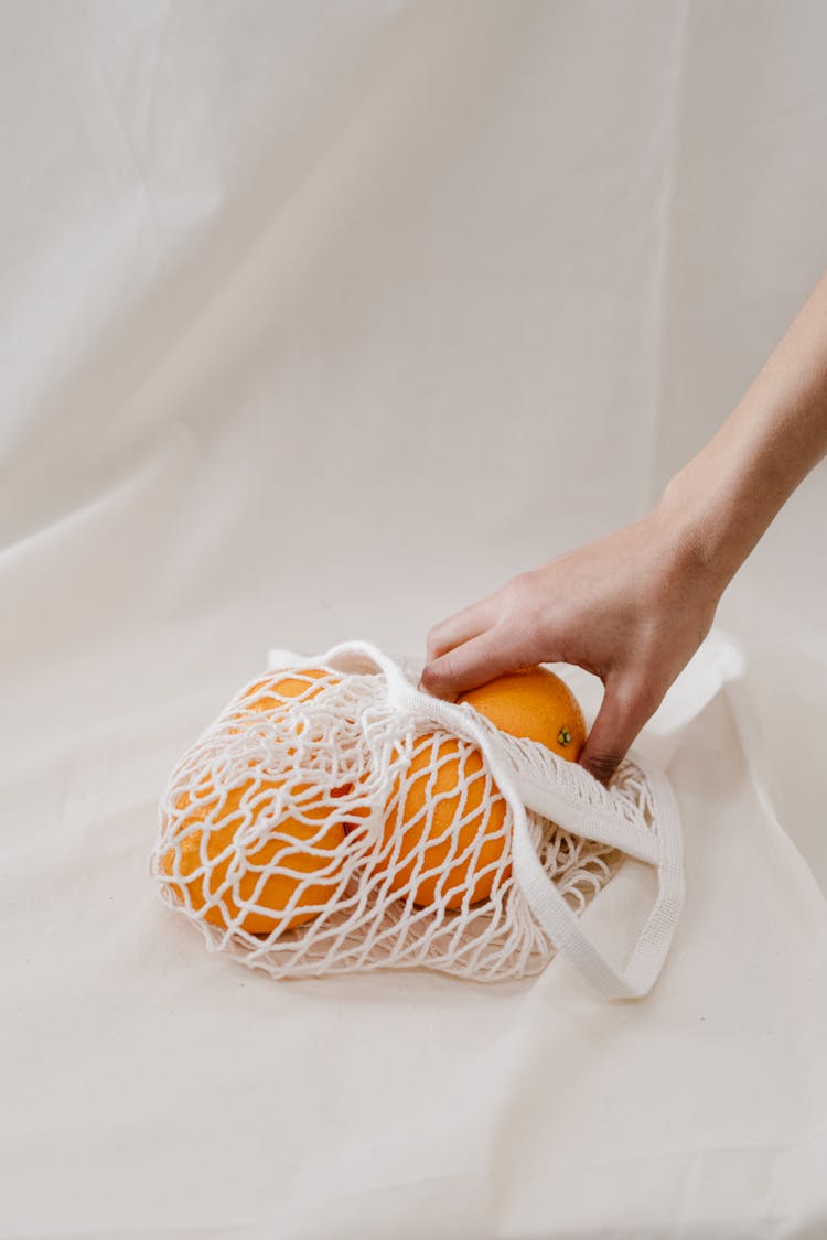 Person Holding Orange Fruit In A White Mesh Bag 