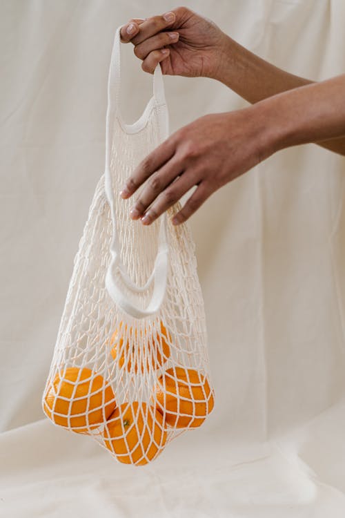 Person Holding Four Oranges in White  Net Bag
