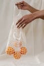 手持一个装满新鲜橙子的可重复使用网袋，背景为中性
