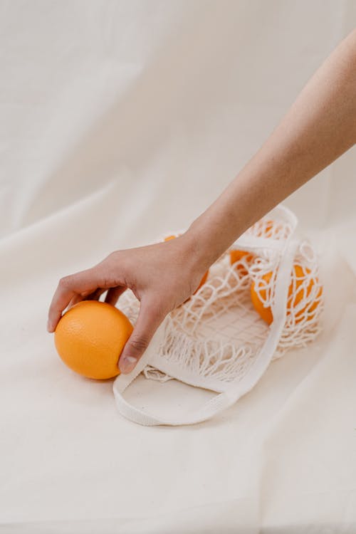 Persona Sosteniendo Fruta Naranja Sobre Textil Blanco