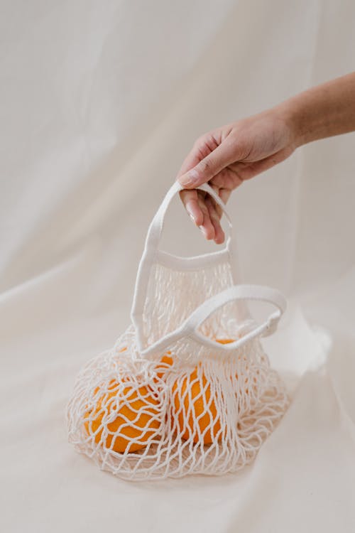 Person Holding Oranges in a White Net Bag 