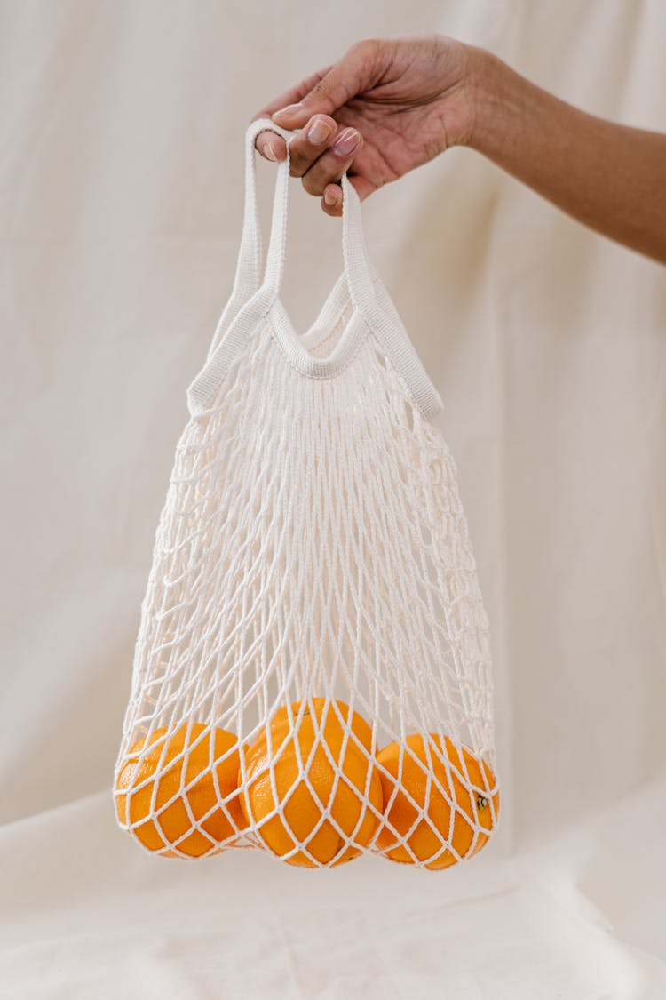 Person Holding Oranges In A White Mesh Bag