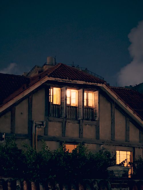 Free Warm glow from windows of a rustic house at night with a tranquil ambiance. Stock Photo