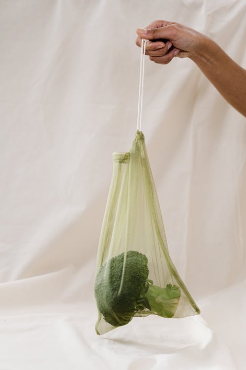 在綠色的塑料袋裡拿著西蘭花的人