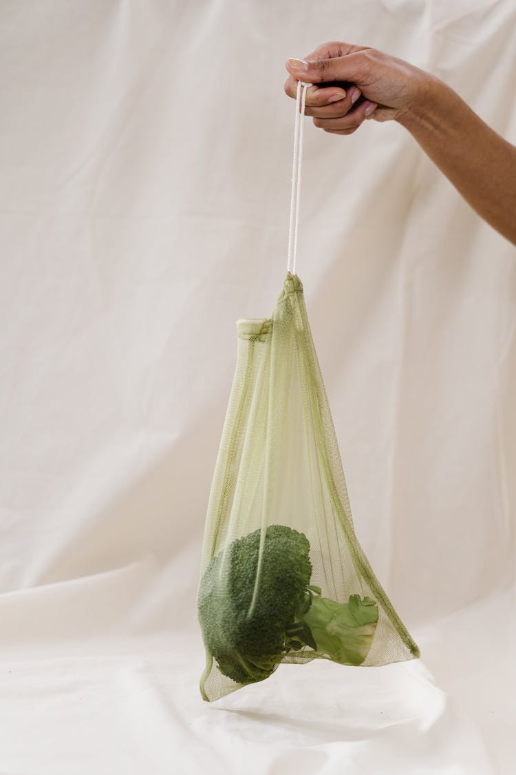 Person Holding A Broccoli In A Green Plastic Bag