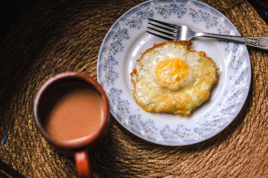A top view of a fried egg on a plate with a cup of coffee, offering a cozy breakfast scene.