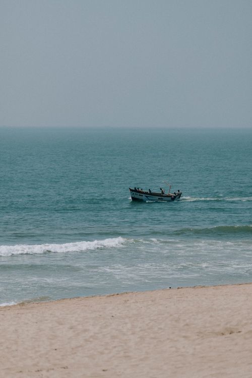 Free A peaceful beach scene with a fishing boat sailing on the calm ocean, ideal for relaxation themes. Stock Photo