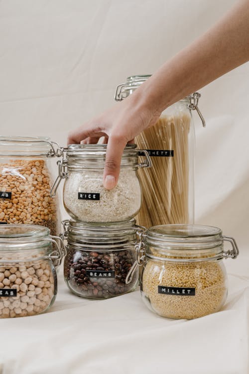 Free Person Holding Clear Glass Jar With Rice Brown and White Beans Stock Photo