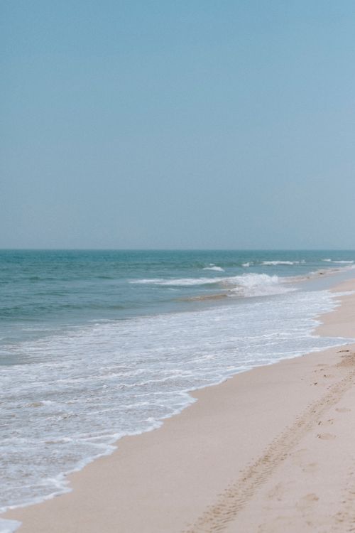 Free A tranquil sandy beach with gentle waves under a clear blue sky, inviting for relaxation. Stock Photo