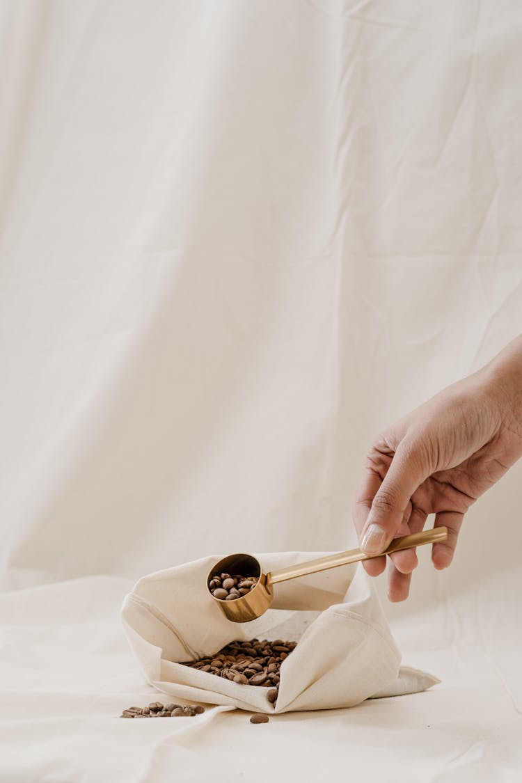 A Person Holding A Scoop With Coffee Beans