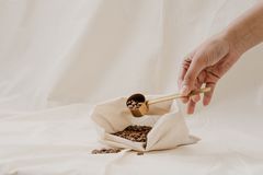 A hand scoops coffee beans from a cloth bag on soft white fabric, perfect for zero waste concept.
