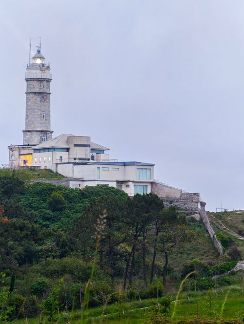 Free Misty view of an ancient lighthouse perched on a lush green cliff. Perfect for travel and nature themes. Stock Photo