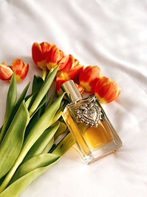 Free A luxurious perfume bottle placed on white fabric surrounded by vibrant orange tulips. Stock Photo