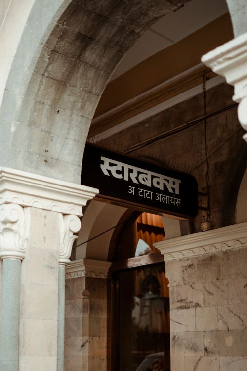 Free A Starbucks sign in Marathi script seen within historic Mumbai architecture. Stock Photo