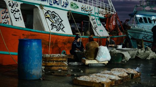 Free Fishermen gather by a colorful boat at a Middle Eastern fishing harbor during dusk. Stock Photo