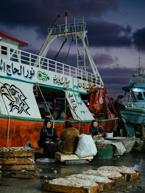 Free Fishermen sorting fresh catch at dusk near a vibrant fishing boat in the harbor. Stock Photo