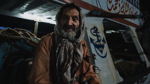 Free An elderly man sits on a traditional fishing boat, showcasing cultural heritage and maritime life. Stock Photo