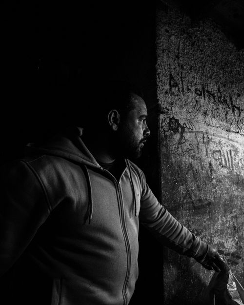 Free A moody black and white image depicting a man in a hoodie gazing thoughtfully at a textured wall. Stock Photo