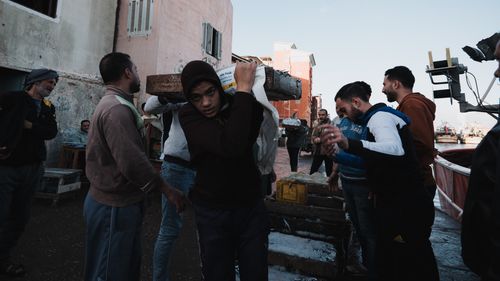Free A bustling scene of fishermen loading supplies at a harbor, showcasing teamwork. Stock Photo