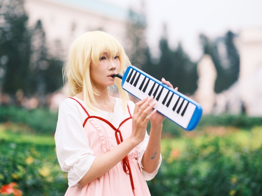 Anime cosplayer plays melodica in a vibrant park setting in Vietnam.