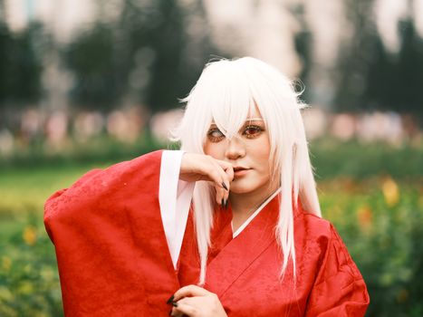 A captivating portrait of anime cosplay with white wig and red robe, set outdoors in Vietnam.
