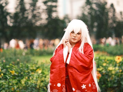 Elegant cosplayer in traditional red attire posing outdoors in a lush Vietnamese garden.